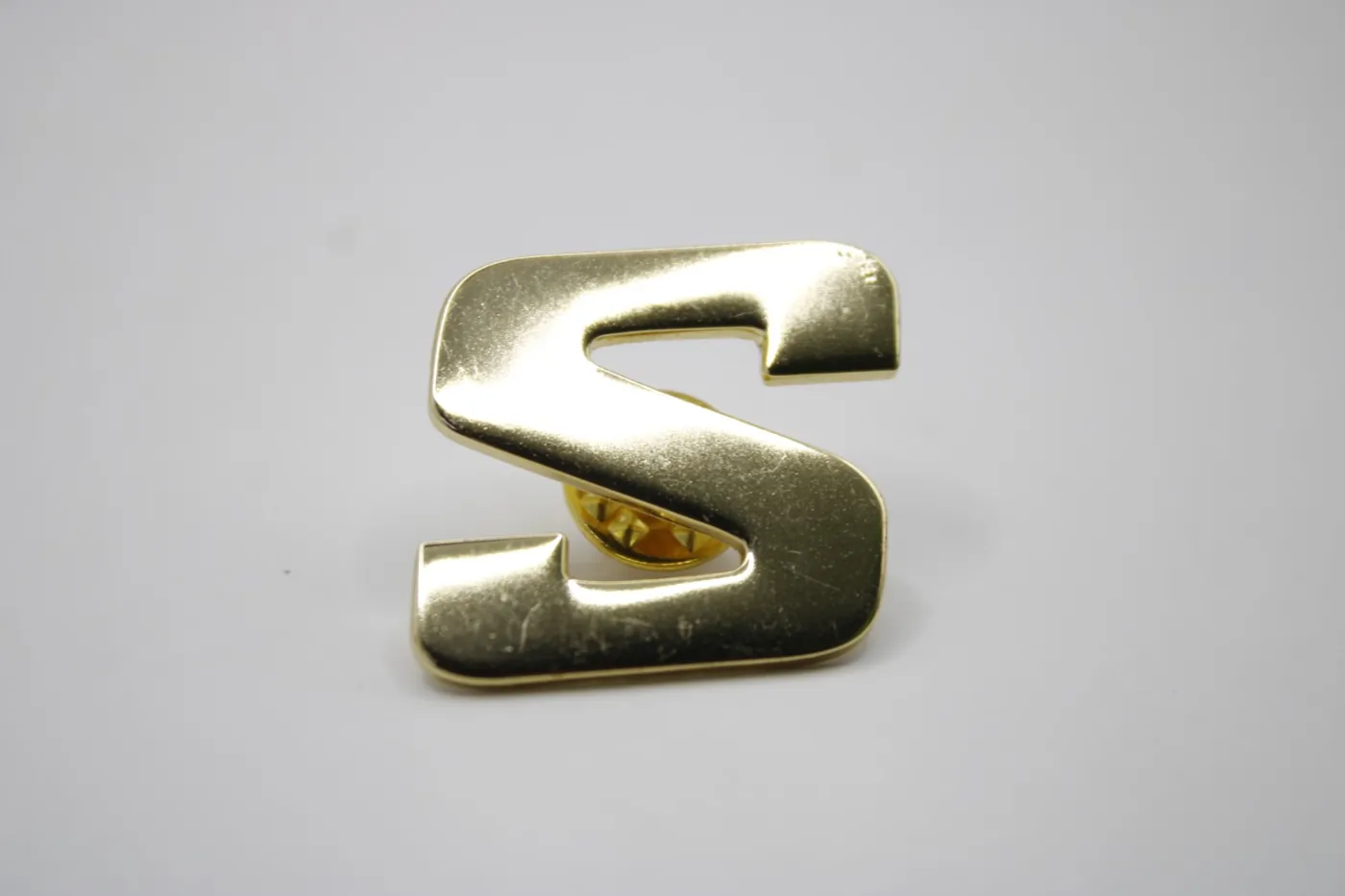 Pin con la letra S en acabado dorado brillante, corte sobre diseño