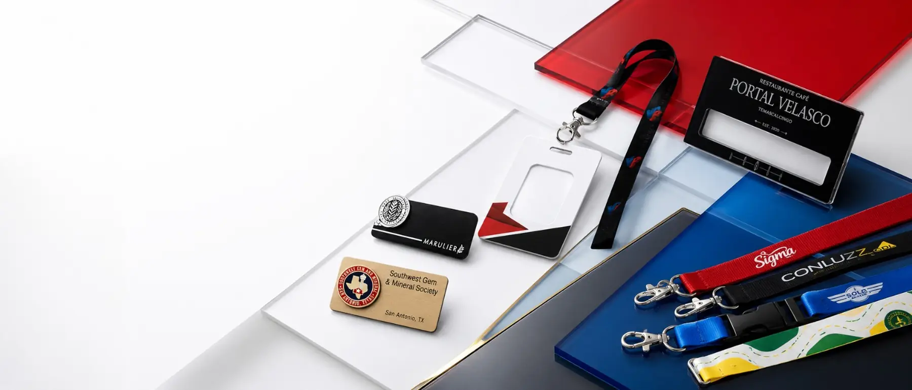 Placas de nombre, portagafete y cordones corporativos sobre placas de acrílico rojo, azul y transparente