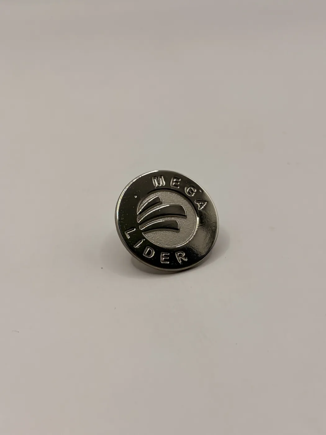 Pin circular metálico oscuro con logotipo grabado del programa Mega Líder