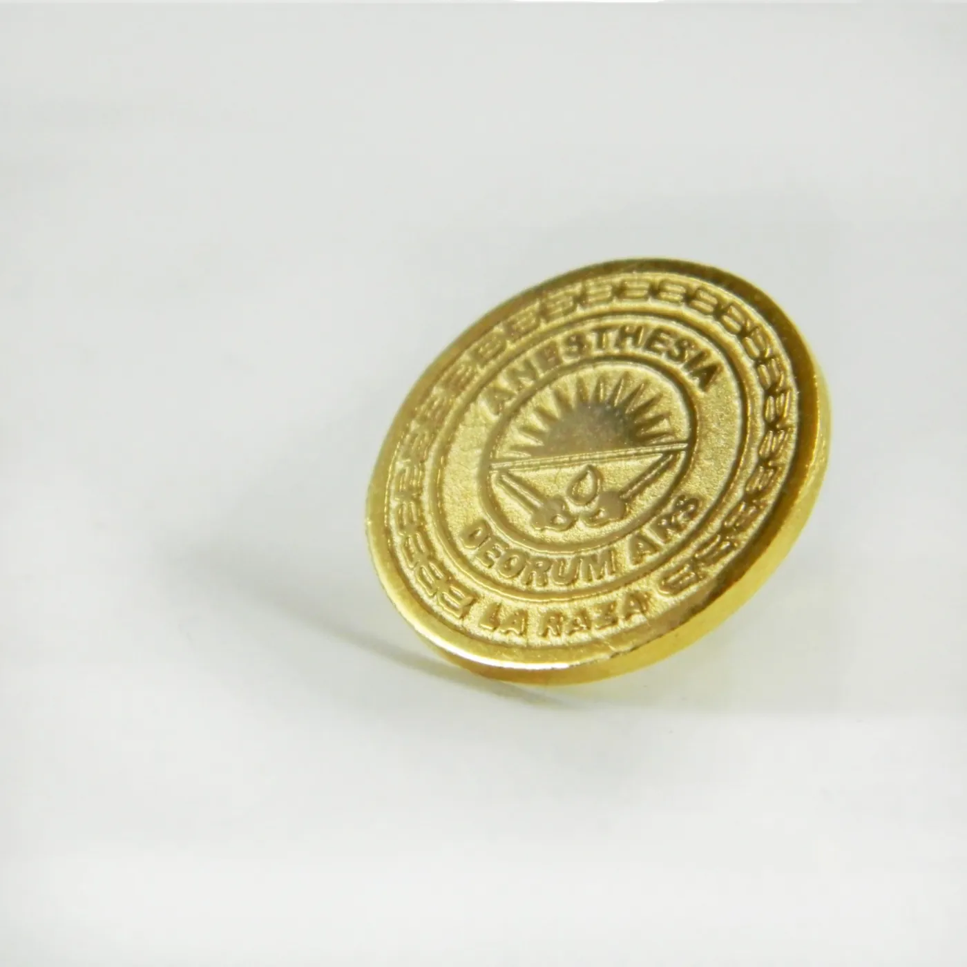 Pin circular dorado con emblema institucional grabado en relieve